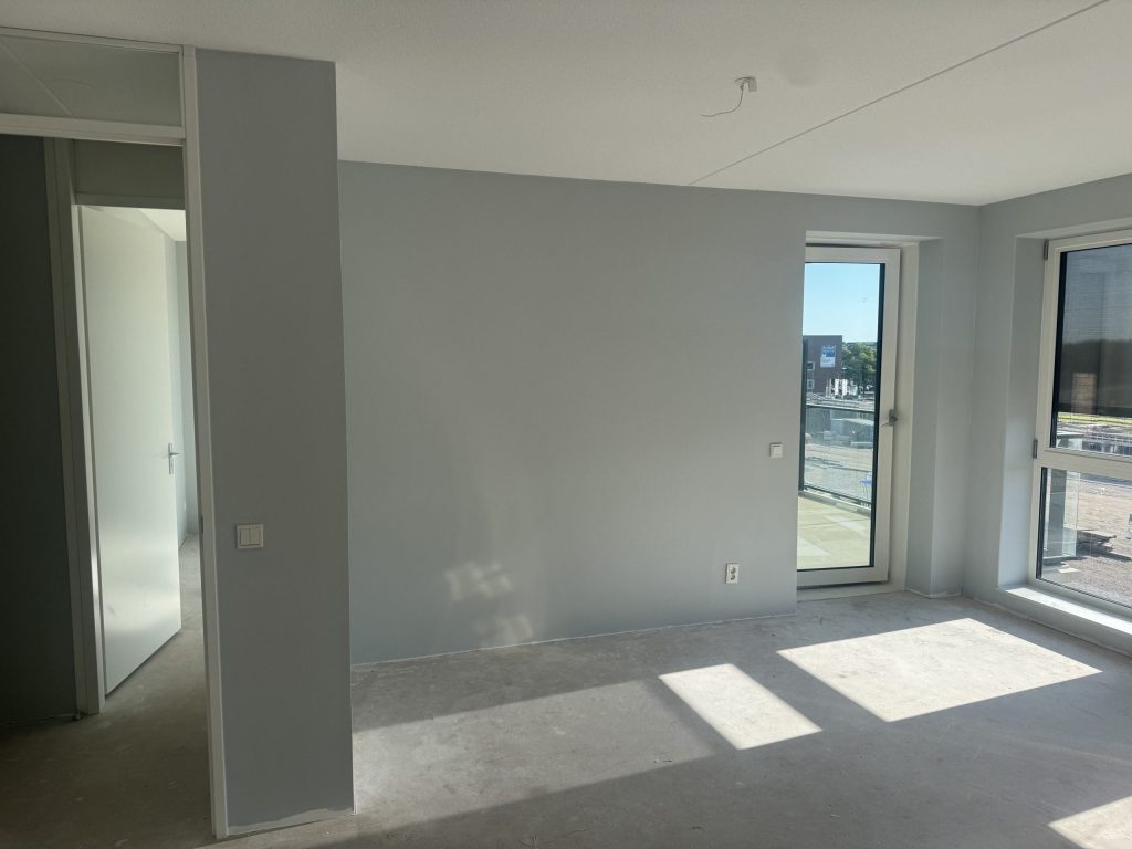 Lichte woonkamer in een nieuw appartement met grijsblauwe wanden en een deur naar het balkon