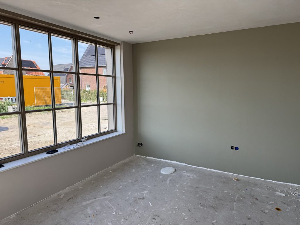 Nieuwbouwkamer met een groot roedenraam en een strak afgewerkte wand in grijsgroen